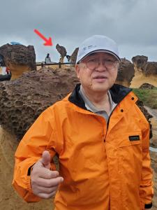 オレンジの上着に帽子を被った市長のアップの後方に赤い矢印がある野柳地質公園での視察の写真