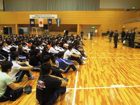 ジャージ姿の大勢の参加者たちが体育館の床で体育座りをして市長の話に耳を傾ける参加者達を横から見た写真