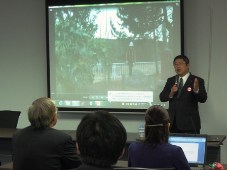 スクリーンに震災の資料を投影し、演壇で講演する市長と、席に座り話に耳を傾ける参加者の写真