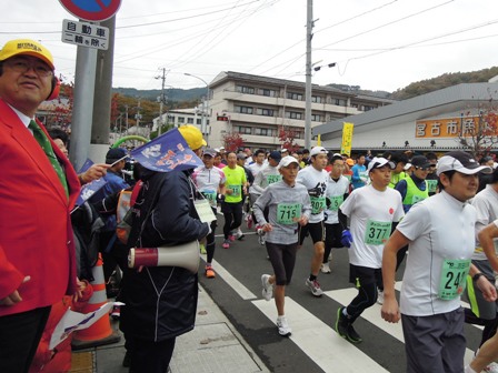 ゼッケンを付けた参加者たちが道路を走っており、沿道でジャケットを着て耳当てを付けた市長の写真
