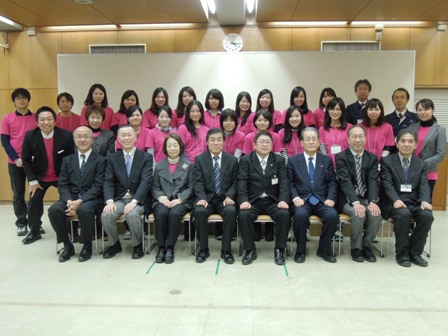 市役所庁舎で、市長と関係者、ピンク色のTシャツを着た実践女子大学の皆さんが横並びに3列で並んで集合している写真