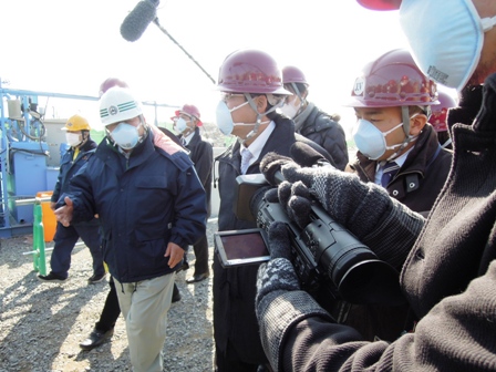ヘルメットを着用した松井一郎知事と市長が歩きながら話をしているところをカメラマンが撮影している写真