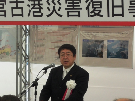 左胸に胸章リボンをつけている市長がマイクの前で話をしている写真