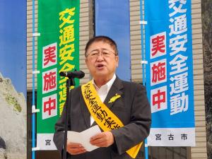 「交通安全運動実施中」と書かれた幟の前で、黄色い襷を体にかけて話をする様子の市長の写真