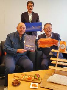 宮古トラウトサーモンの大きな切り身を両手で持つ市長と関係者の男性2名が写った記念写真
