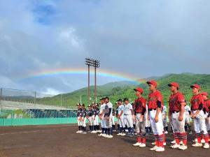 グラウンドに整列した選手たちの空の奥に虹が架かっている写真