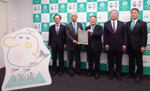 宮古市のバックパネルをバックに5名の関係者が並び、左から2番目の男性と3番目の市長が寄附金を持ち、その前にデカポンのイラストパネルが置かれている記念撮影の写真