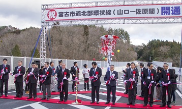 新しい道路の上に「祝 宮古市道北部環状線（山口－佐原間）開通」の横断幕が掲げられ、市長と関係者がテープカットをしている写真
