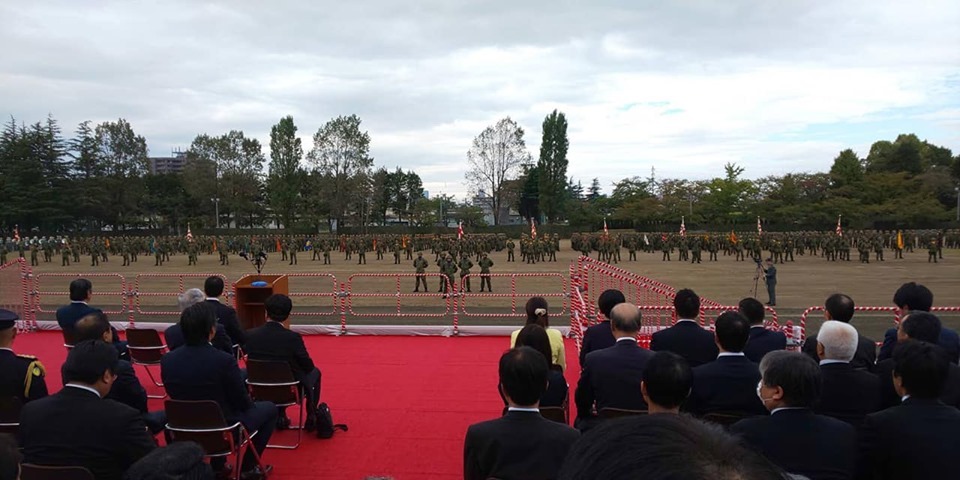 赤いじゅうたんが敷かれた客席に関係者が座り、正面で迷彩服を着た隊員の方々が整列している様子を関係者の後方から撮影した写真
