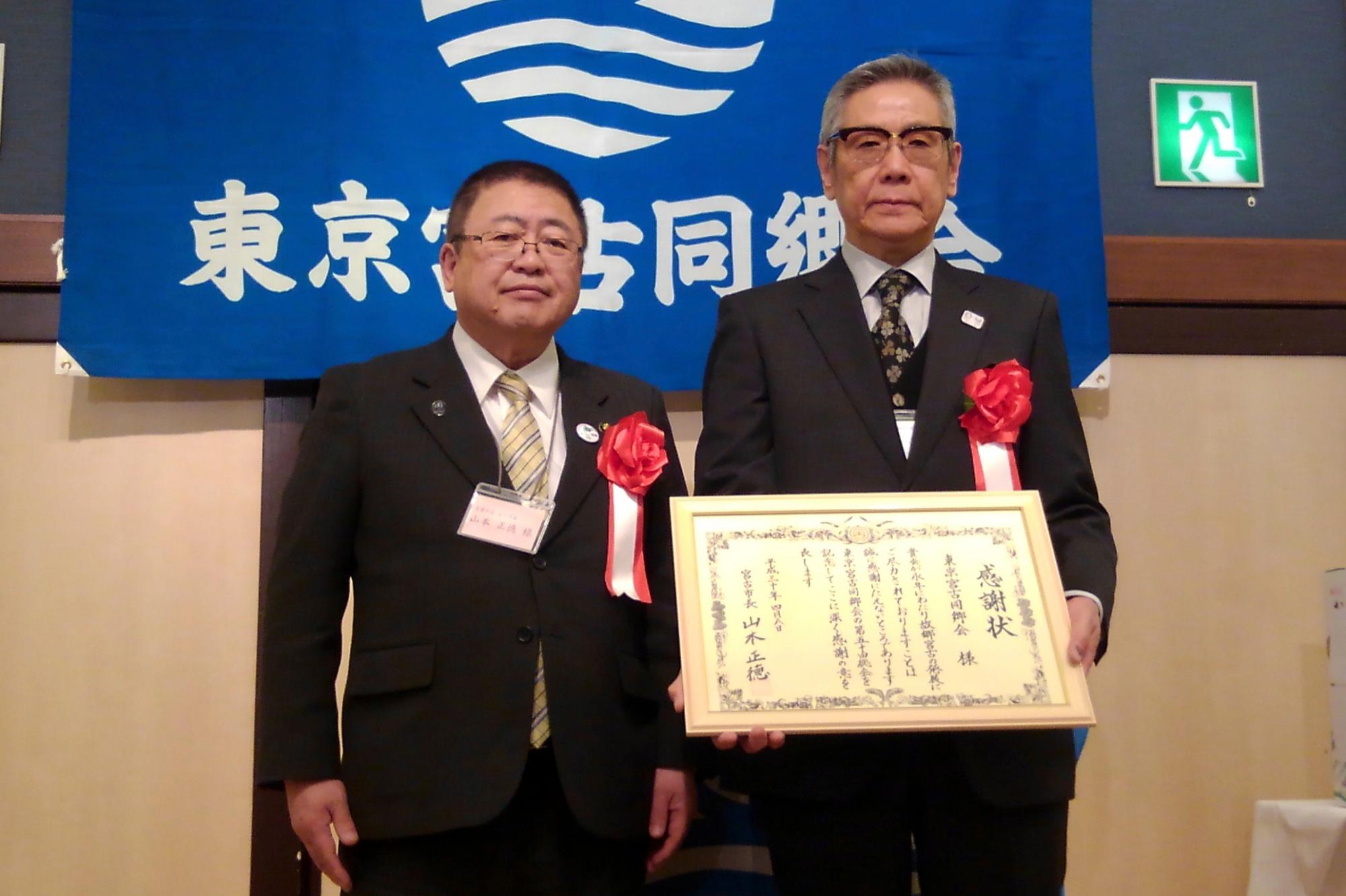 「東京宮古同郷会」と書かれた団旗の前で胸章をつけた市長と手に賞状を持っている白土正治会長が並び記念撮影している写真