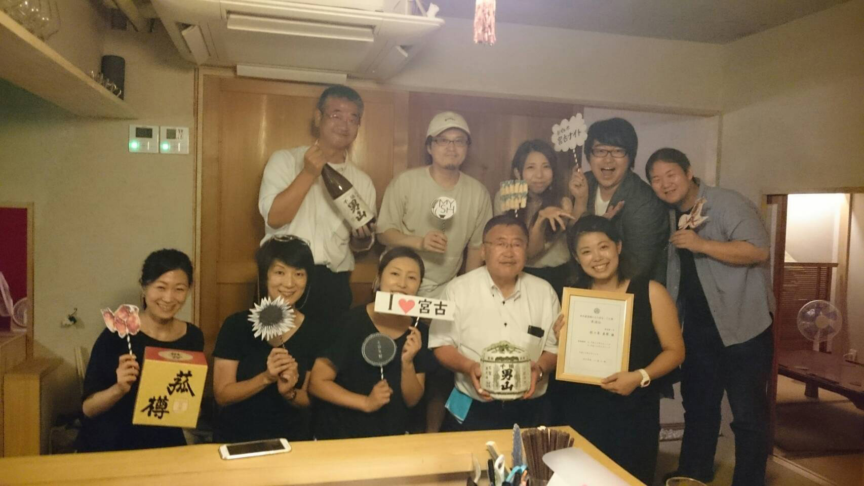 お酒やフォトプロップスや賞状を手に持った、市長と関係者が記念撮影している写真