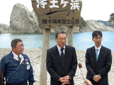後方に海と白い大きな岩が見える浄土ヶ浜の看板前で、長浜博行環境大臣と園田康博副大臣と市長が並んでおり、傾けられたマイクに向けて話をする様子の写真