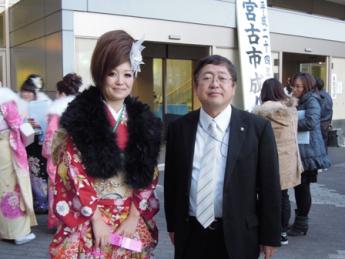 赤い振袖に黒いファーのショールをかけた女性と市長が記念撮影している写真