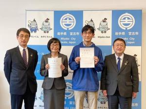 バックパネルの前で、両手で委嘱状を持った松下さんと中村さんを中央に、市長と副市長が横一列に並んでいる写真
