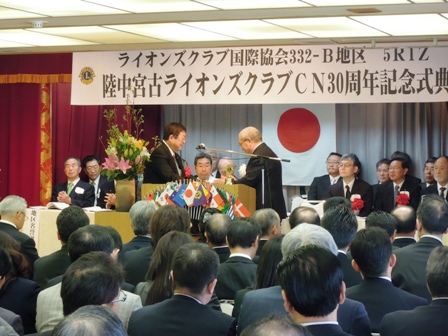 「ライオンズクラブ国際協会332-B地区5RTZ陸中宮古ライオンズクラブCN30周年記念式典」と書かれた舞台看板があり、演壇で表彰しているのを椅子に座っている参加者達が見守っている写真