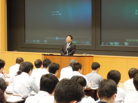 総務省自治大学校の講義室の演壇で、講義を行う市長と話を聞く参加者の写真