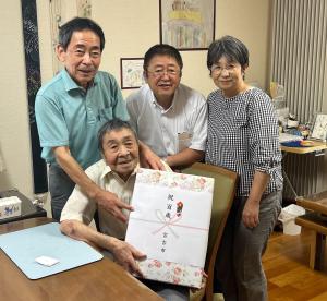お祝いの品を持った小野寺繁夫さんとご家族2名と市長の記念写真