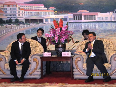 中央に置かれた演題花の左右に並んで座っている市長と烟台市の関係者の写真