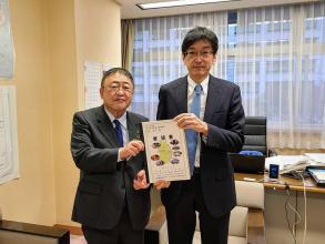 レースのカーテンがひかれた室内で、国土交通省の高田昌行技術総括審議官と市長が要望書を一緒に持ち並んでいる写真