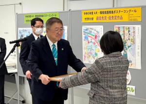 ポスター作品の前で女性が市長から表彰状を受け取っている写真