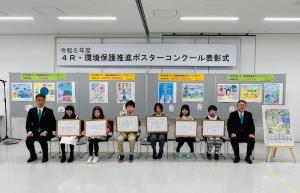 4R・環境保護推進ポスターコンクール表彰式で入賞した作品の前に作者6名が座り、右端に市長、左端に関係者の方が座り記念撮影をしている写真