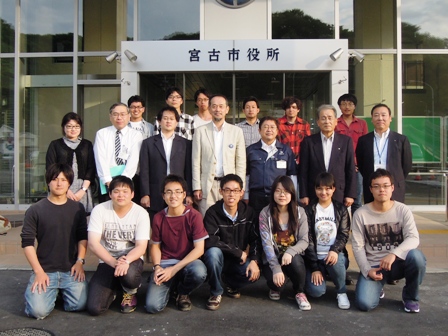 宮古市役所と書かれた入口の前で市長や関係者や学生達が3列に並び記念撮影している写真