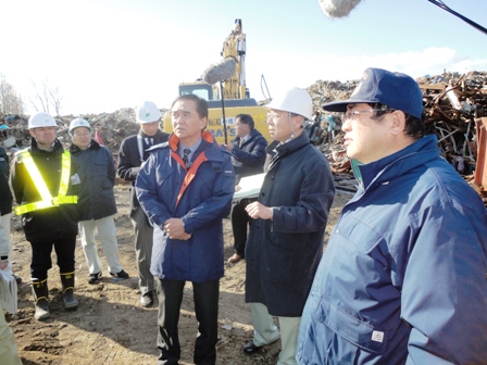 がれきが多く積まれた場所で作業服をきた男性達と関係者の男性が話しているのを市長がきいている写真