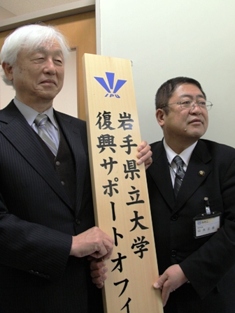「岩手県立大学復興サポートオフィス」と書かれた木製の縦看板を市長と中村慶久学長が手に持っている写真