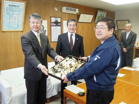 市長が小松敬一局長より中尊寺ハスの株がのっている入れ物を渡すところを記念撮影している写真