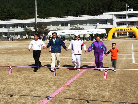 市長と男性2名、女性1名、子供1名が全員で手をつなぎ横一列になってゴールテープに向かい走っている様子の写真