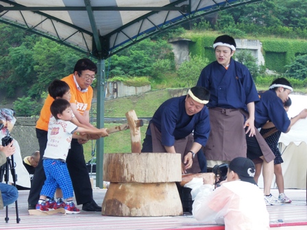 特設ステージの上で杵を男の子2人と市長が一緒に持って、餅つきをしている写真