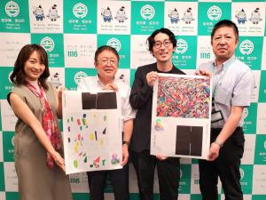 松田文登代表取締役副社長と矢野智美岩手コミュニティ―マネージャーと市長と関係者の男性が宮古市の会見パネルの前でアート作品のようなものを持って並んでいる写真