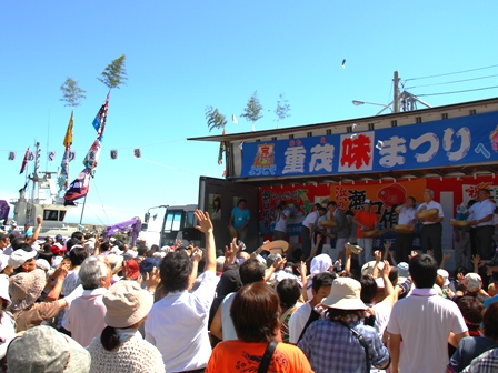特設ステージの正面に「重茂味まつり」と書かれた横断幕があり、ステージの前にたくさんのお客さんが集まっている写真