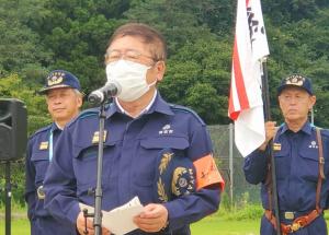 消防隊の制服を着た市長がスタンドマイクの前に立ち話をしている様子の写真