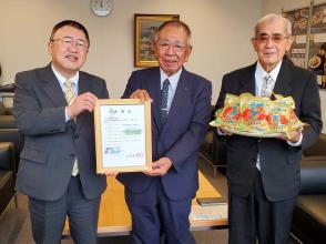個別包装された黒糖がたくさん載せてあるお盆を持った宮古製糖の代表の男性と、市長と一緒に額に入った感謝状を持っている社長が横一列に並んでいる記念写真