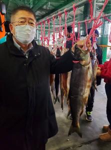 ひもで吊るされたたくさんの鮭の1匹のひもを持ちながらが宮古鮭まつりを楽しんでいる市長の写真