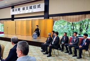 第8期 叡王就位式会場で、ステージ上の金屏風の前に座る藤井叡王とステージ横に座る関係者らの写真
