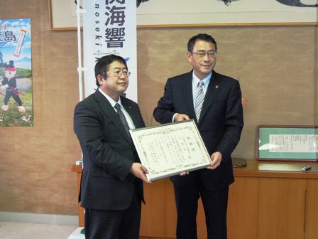 応接室のような部屋で市長と中尾友昭市長が、額縁に入った感謝状を手に持っている写真