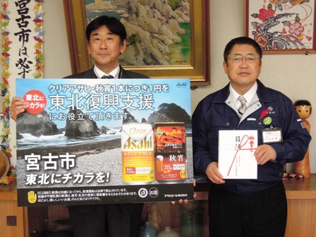 市長と関係者が横並びに立っており、市長は目録を手に持ち、関係者は「東北復興支援」と書かれたアサヒビールの写真パネルを手に持っている写真