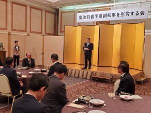「菊池哲前岩手県副知事を慰労する会」と書かれた横断幕が吊るされ、金屏風が置かれた舞台上で、スタンドマイクに向かい話をする様子の市長の写真