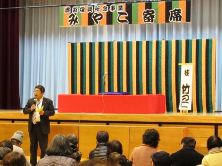 「みやこ寄席」と書かれた吊り看板と定式幕が張られており、赤の高座が設置された舞台下で、市長がマイクを持ち参加者に向けて話をしている写真