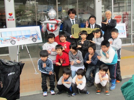 市長と小学生くらいの子供たち、関係者とウルトラマンが両手をクロスにしたポーズを取っている写真