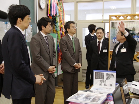 学校の教室内で谷川浩司会長、森内俊之名人、羽生善治三冠が、市長の話に耳を傾ける様子の写真