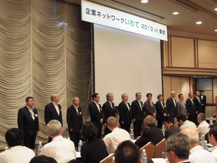 「企業ネットワークいわて2013 in 東京」の吊り看板があるステージ上に立つ市長と関係者13人が並んでいる写真