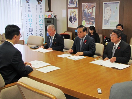 木製のテーブルの席に向かい合わせで座る男性と市長を含む3名の男性たちが手元の資料を見ながら話をしている様子の写真