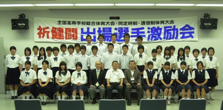 「全国高等学校総合体育大会・同定時制・通信制体育大会 祈健闘出場選手激励会」と書かれた横断幕の前に男女代表選手達が3列に並び市長達と記念撮影している写真