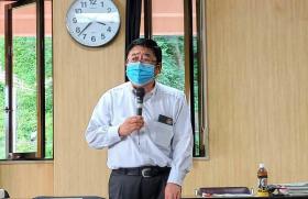 マスク姿の市長が資料が置かれたテーブルの前に立ち、片手でマイクを持ちながら説明をしている写真