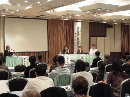 ホテルのステージの来賓席に市長や関係者が座っており、並べられた椅子に座って話を聞く参加者の写真