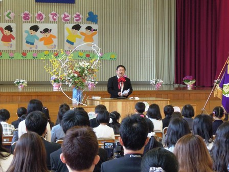 椅子に座る新入生の前で演壇に立ち、話をする市長を保護者席から見た写真