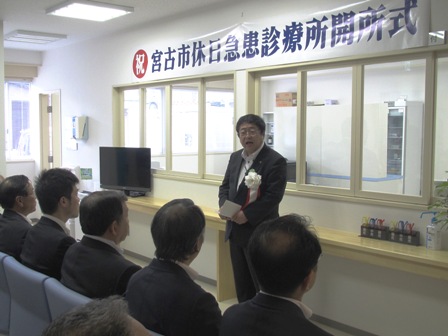 「宮古市休日急患診療所開所式」の横断幕の下、挨拶する市長と、椅子に座る関係者の写真